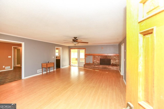 unfurnished living room with wood-type flooring, ornamental molding, ceiling fan, and a fireplace