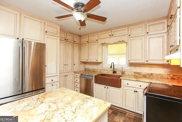 kitchen with light stone counters, stainless steel appliances, sink, and cream cabinetry