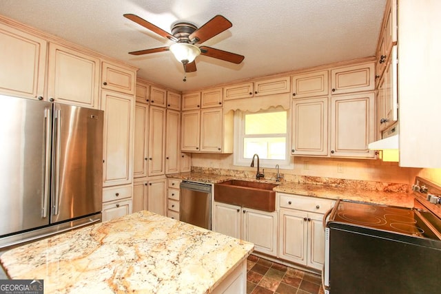 kitchen featuring appliances with stainless steel finishes, cream cabinets, sink, light stone countertops, and a textured ceiling