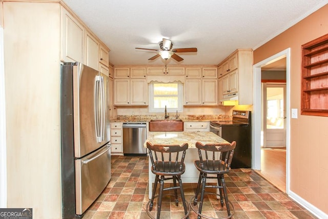 kitchen with sink, a breakfast bar area, a kitchen island, stainless steel appliances, and cream cabinetry