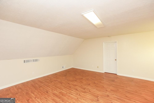 additional living space featuring hardwood / wood-style flooring, vaulted ceiling, and a textured ceiling