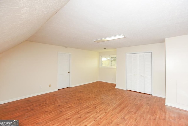 bonus room featuring lofted ceiling, a textured ceiling, and light hardwood / wood-style floors