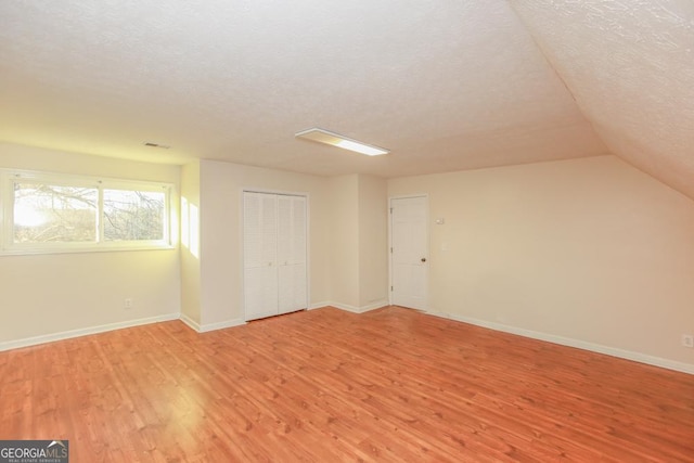 additional living space with lofted ceiling, a textured ceiling, and light wood-type flooring