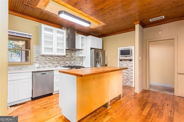 kitchen featuring wall chimney exhaust hood, butcher block counters, a kitchen island, stainless steel appliances, and white cabinets