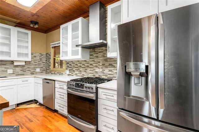 kitchen with light hardwood / wood-style flooring, appliances with stainless steel finishes, white cabinets, wall chimney range hood, and backsplash