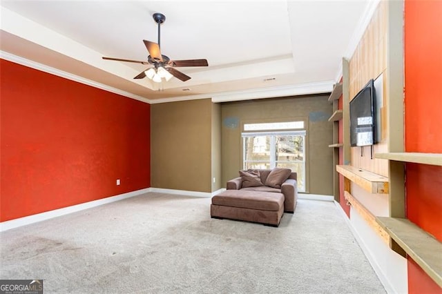 living area featuring ceiling fan, ornamental molding, a raised ceiling, and carpet