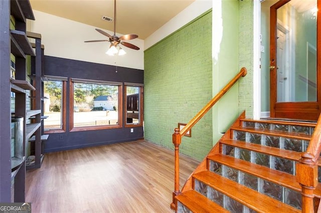 staircase with ceiling fan, brick wall, wood-type flooring, and a high ceiling