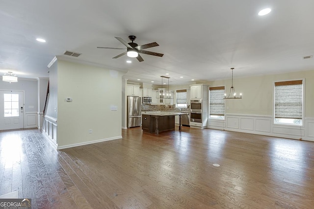 unfurnished living room with hardwood / wood-style flooring, ornamental molding, and ceiling fan with notable chandelier