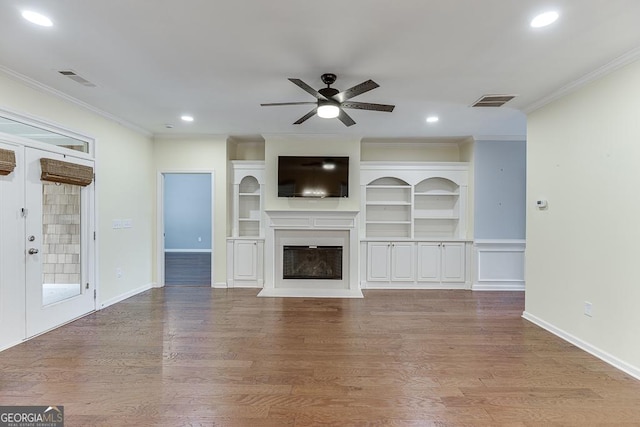 unfurnished living room with wood finished floors, a glass covered fireplace, visible vents, and crown molding