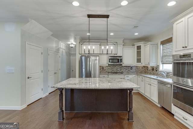 kitchen with light stone counters, decorative light fixtures, a center island, ornamental molding, and stainless steel appliances