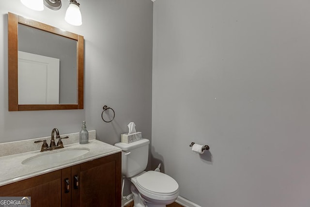 half bath with toilet, baseboards, and vanity