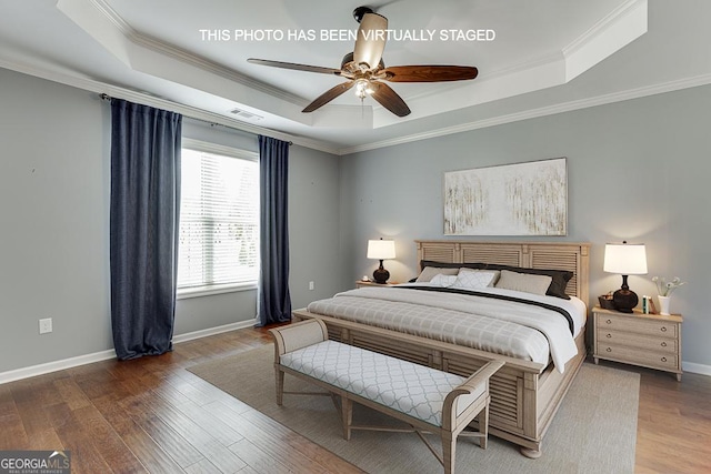 bedroom with a tray ceiling, visible vents, ornamental molding, wood finished floors, and baseboards