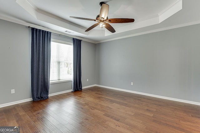 spare room with a tray ceiling, visible vents, baseboards, and wood finished floors