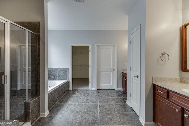 full bathroom with visible vents, vanity, a bath, a stall shower, and a walk in closet