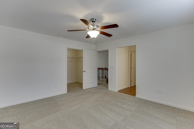 unfurnished bedroom with a walk in closet, light colored carpet, ceiling fan, and a closet