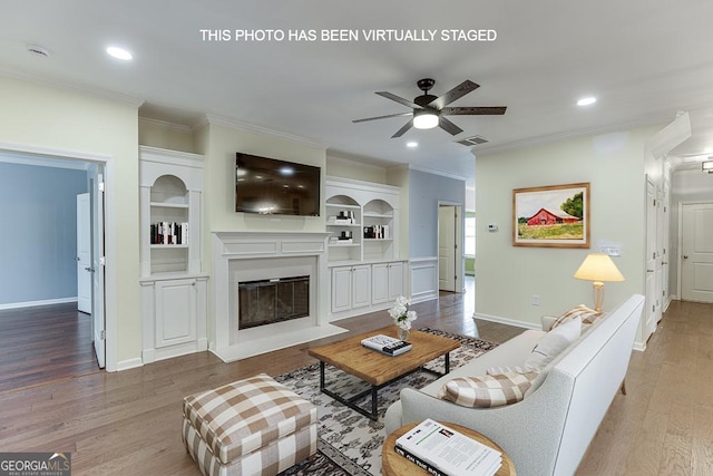 living room with visible vents, a ceiling fan, a glass covered fireplace, ornamental molding, and wood finished floors