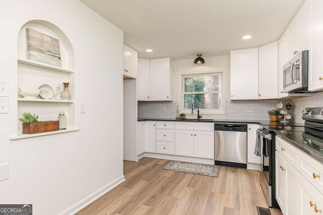 kitchen featuring white cabinetry, light hardwood / wood-style flooring, dark stone countertops, and appliances with stainless steel finishes