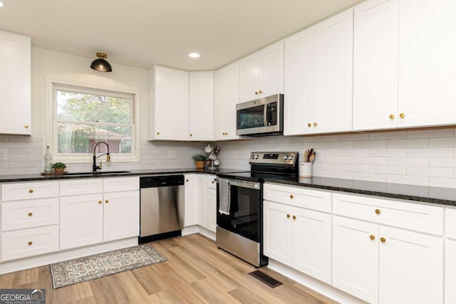 kitchen with dark stone countertops, light hardwood / wood-style floors, white cabinets, and appliances with stainless steel finishes