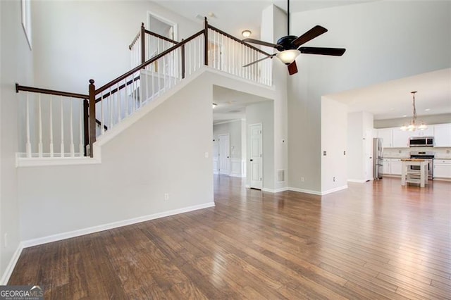 unfurnished living room featuring dark wood-type flooring, ceiling fan with notable chandelier, and a high ceiling