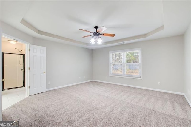 unfurnished room with a raised ceiling, light colored carpet, and ceiling fan