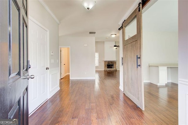 foyer entrance featuring dark hardwood / wood-style floors, a fireplace, ornamental molding, ceiling fan, and a barn door