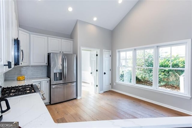 kitchen with white cabinets, decorative backsplash, stainless steel appliances, light stone countertops, and light wood-type flooring