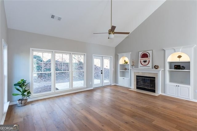 unfurnished living room with hardwood / wood-style floors, built in features, high vaulted ceiling, ceiling fan, and french doors