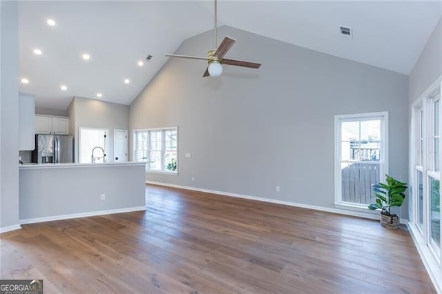 unfurnished living room with high vaulted ceiling, plenty of natural light, light hardwood / wood-style floors, and ceiling fan