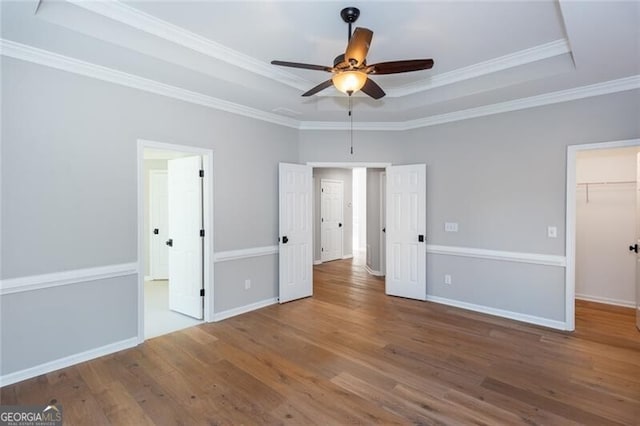 unfurnished bedroom featuring crown molding, hardwood / wood-style flooring, a walk in closet, and a raised ceiling