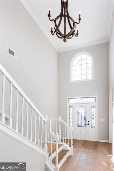 foyer featuring crown molding, a towering ceiling, light hardwood / wood-style floors, and a notable chandelier