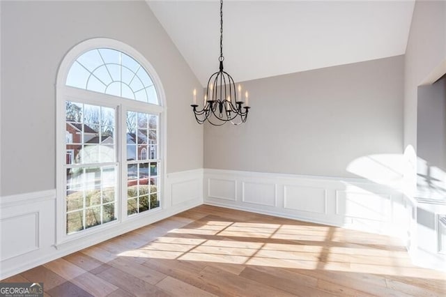 unfurnished dining area featuring lofted ceiling, a chandelier, and hardwood / wood-style floors