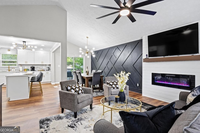 living room featuring ceiling fan with notable chandelier, high vaulted ceiling, light hardwood / wood-style floors, and a textured ceiling