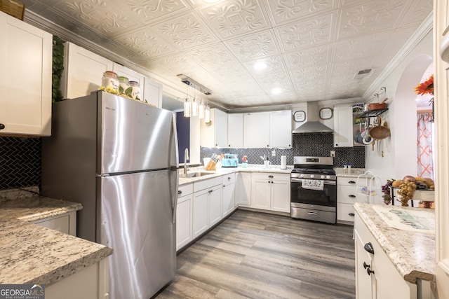 kitchen featuring sink, white cabinetry, decorative light fixtures, stainless steel appliances, and wall chimney range hood