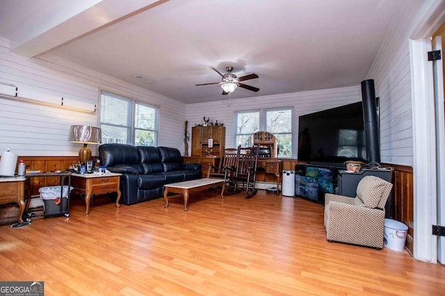 living room featuring beamed ceiling, light hardwood / wood-style floors, ceiling fan, and a wood stove