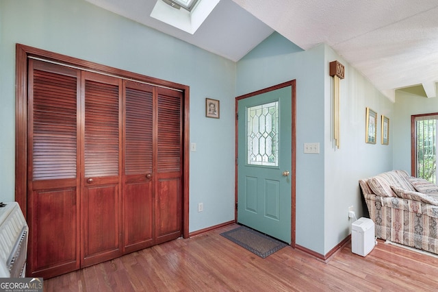 entryway featuring lofted ceiling with skylight, heating unit, and light wood-type flooring