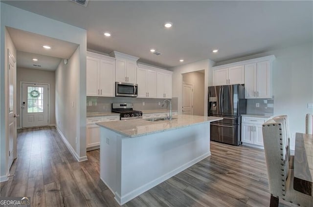 kitchen with stainless steel appliances, white cabinetry, sink, and a center island with sink