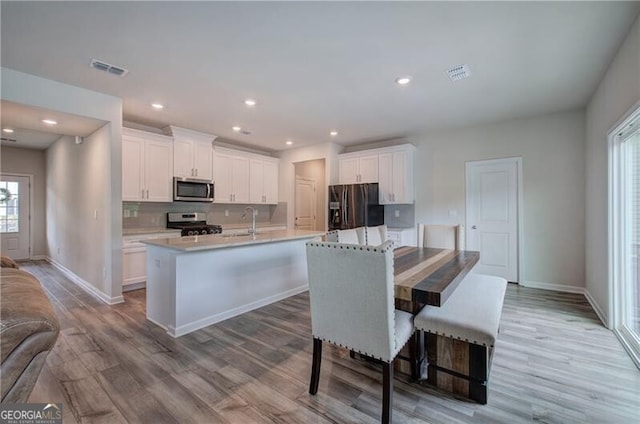 kitchen featuring a breakfast bar, backsplash, stainless steel appliances, an island with sink, and white cabinets