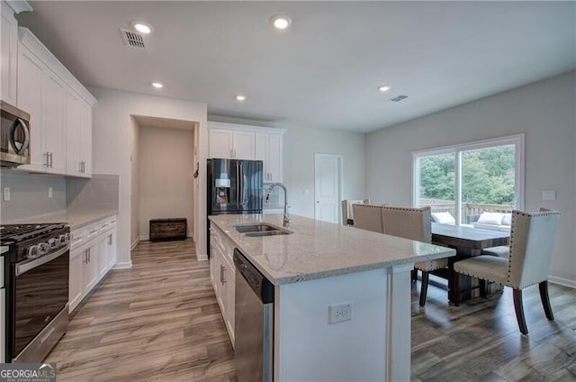 kitchen featuring sink, white cabinetry, light stone counters, appliances with stainless steel finishes, and an island with sink