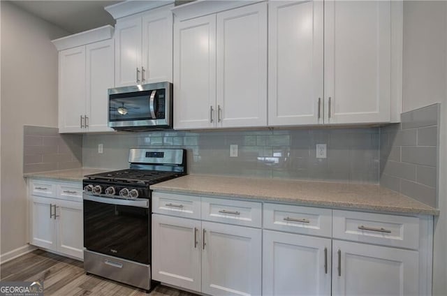 kitchen featuring hardwood / wood-style floors, white cabinetry, decorative backsplash, light stone counters, and stainless steel appliances