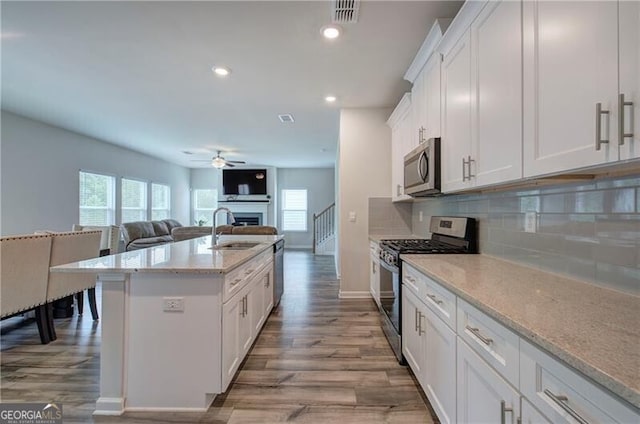 kitchen featuring appliances with stainless steel finishes, sink, white cabinets, decorative backsplash, and a kitchen island with sink