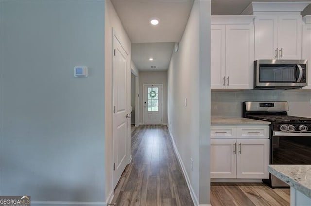 kitchen featuring white cabinetry, tasteful backsplash, light stone counters, light wood-type flooring, and appliances with stainless steel finishes