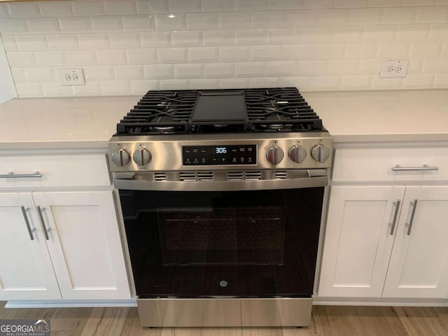 kitchen featuring white cabinetry, decorative backsplash, stainless steel gas range oven, and light hardwood / wood-style flooring