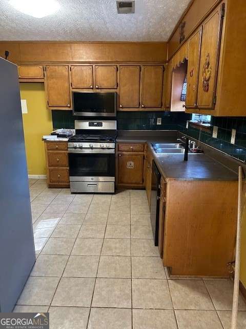 kitchen with light tile patterned flooring, stainless steel appliances, sink, and a textured ceiling