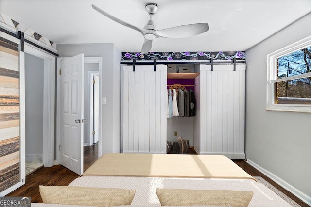 bedroom with a barn door, dark wood-type flooring, ceiling fan, and a closet