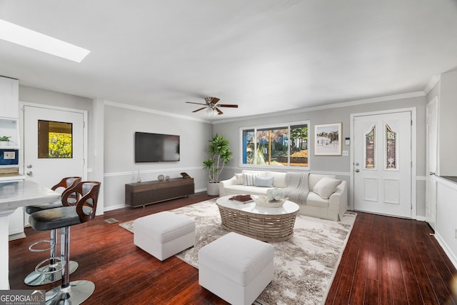 living room with dark wood-type flooring, ceiling fan, ornamental molding, and a skylight