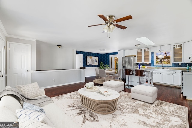 living room with sink, crown molding, dark wood-type flooring, ceiling fan, and a skylight