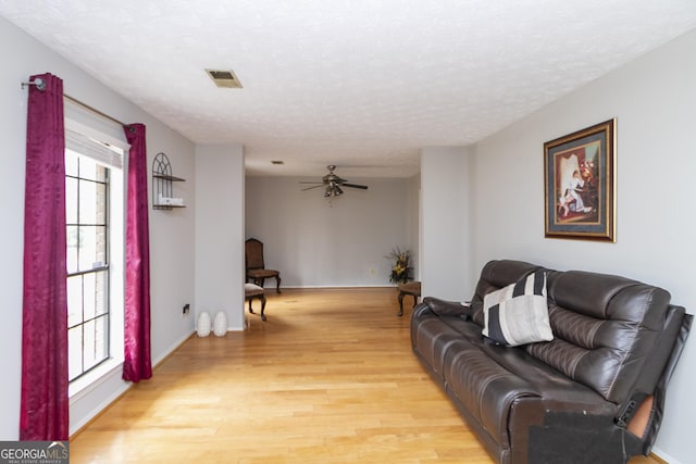 living room with ceiling fan, light hardwood / wood-style floors, and a textured ceiling