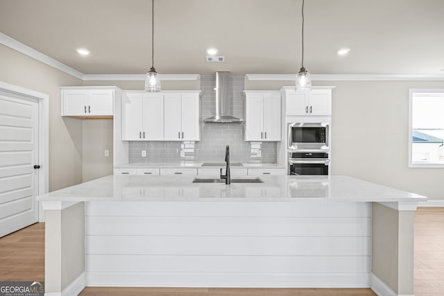 kitchen with hanging light fixtures, a large island with sink, stainless steel appliances, light stone countertops, and wall chimney exhaust hood