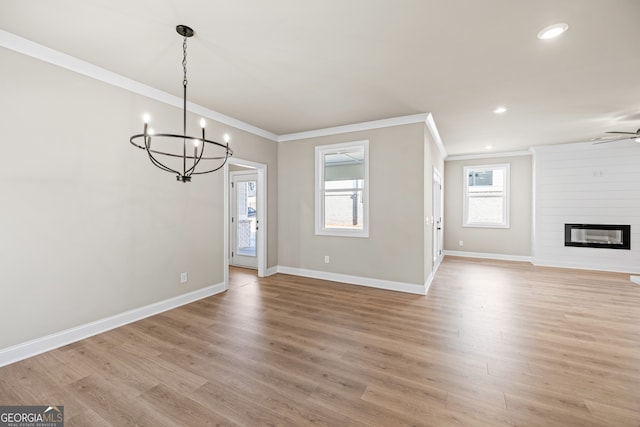 unfurnished dining area featuring crown molding, light hardwood / wood-style flooring, a large fireplace, and ceiling fan with notable chandelier