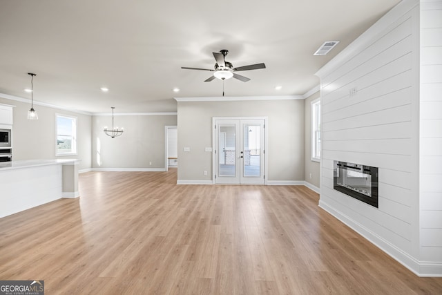 unfurnished living room with french doors, crown molding, light wood-type flooring, a fireplace, and ceiling fan with notable chandelier